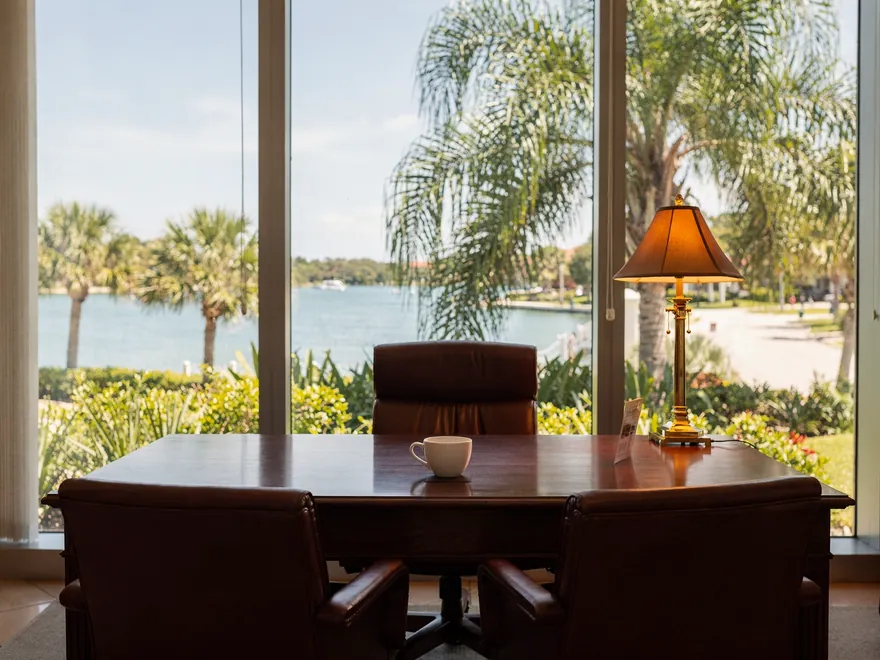 Advisory office with a walnut desk and leather chairs facing palms and a calm bay, Naples