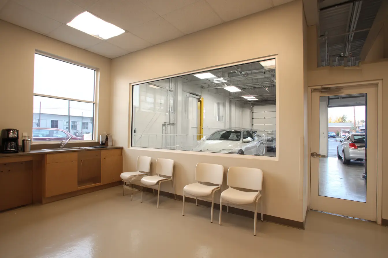 A tidy auto shop waiting room with chairs, a coffee station and a window onto the service bays