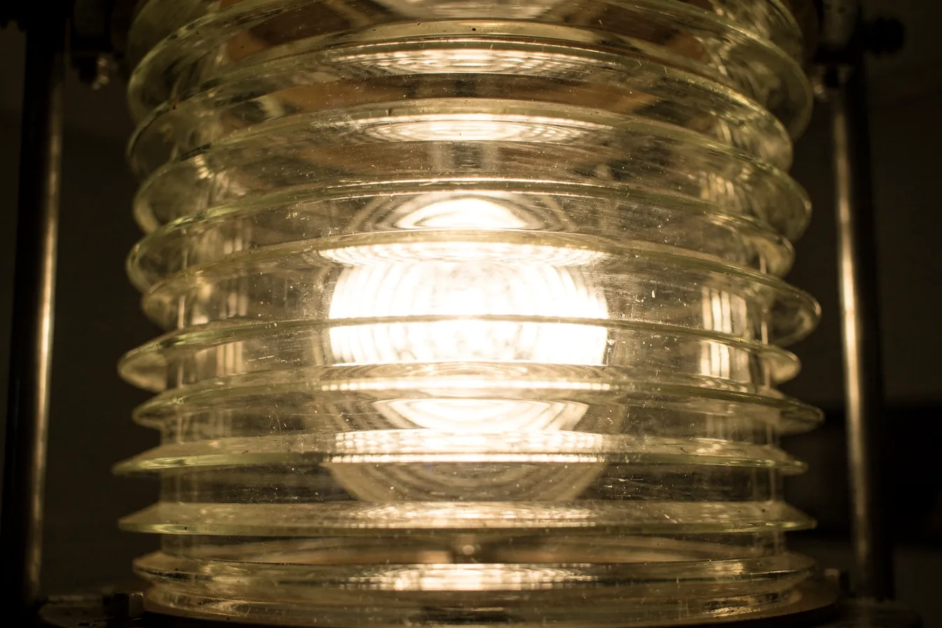 A large glass lighthouse lens glowing softly in a dark room