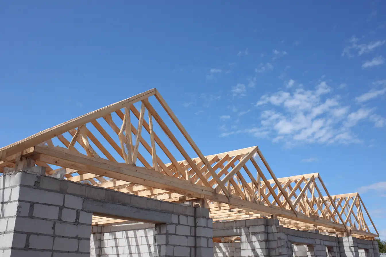 New wooden roof trusses set on the concrete block walls of a home under construction, a clear blue sky above