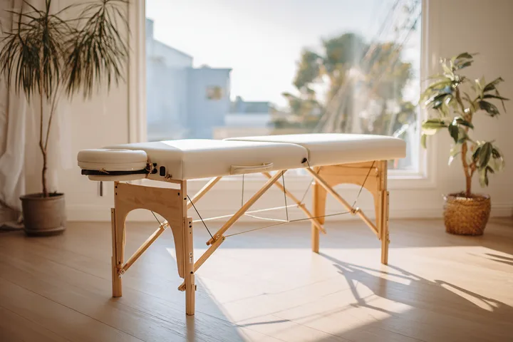 An empty treatment table in a bright room with plants and a window onto palms