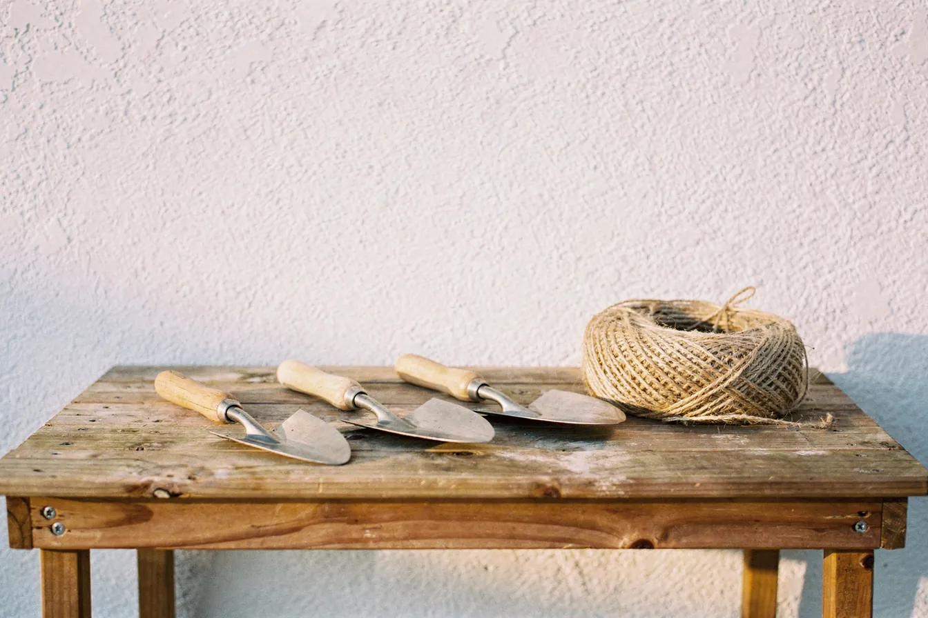 Worn hand tools hanging on a pegboard above a wooden workbench in warm light