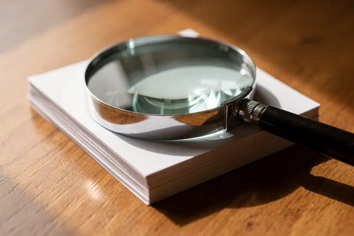A magnifying glass resting on blank paper cards on a wooden table in bright window light