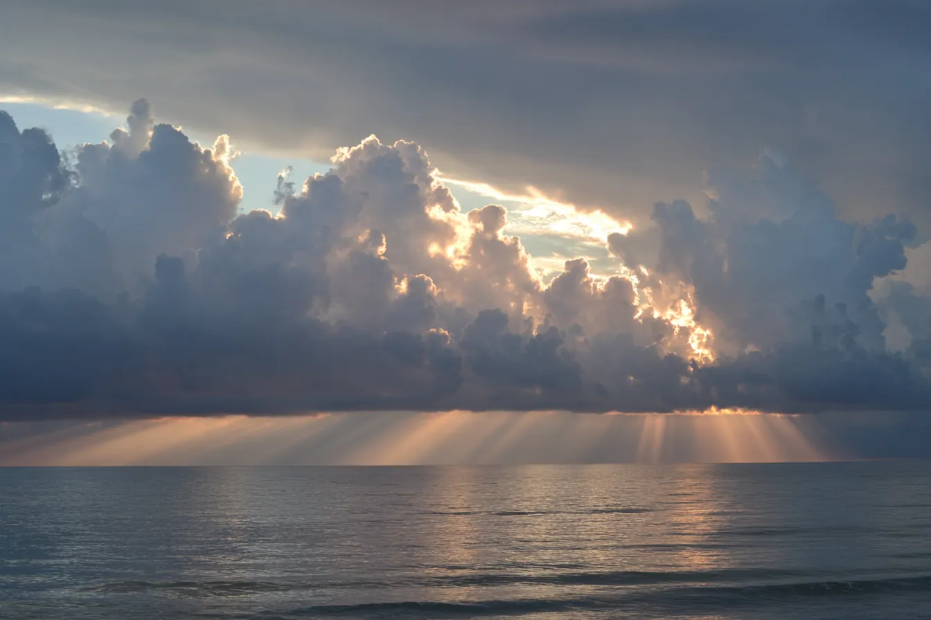 Storm clouds parting over a calm gray sea, rays of light reaching the water