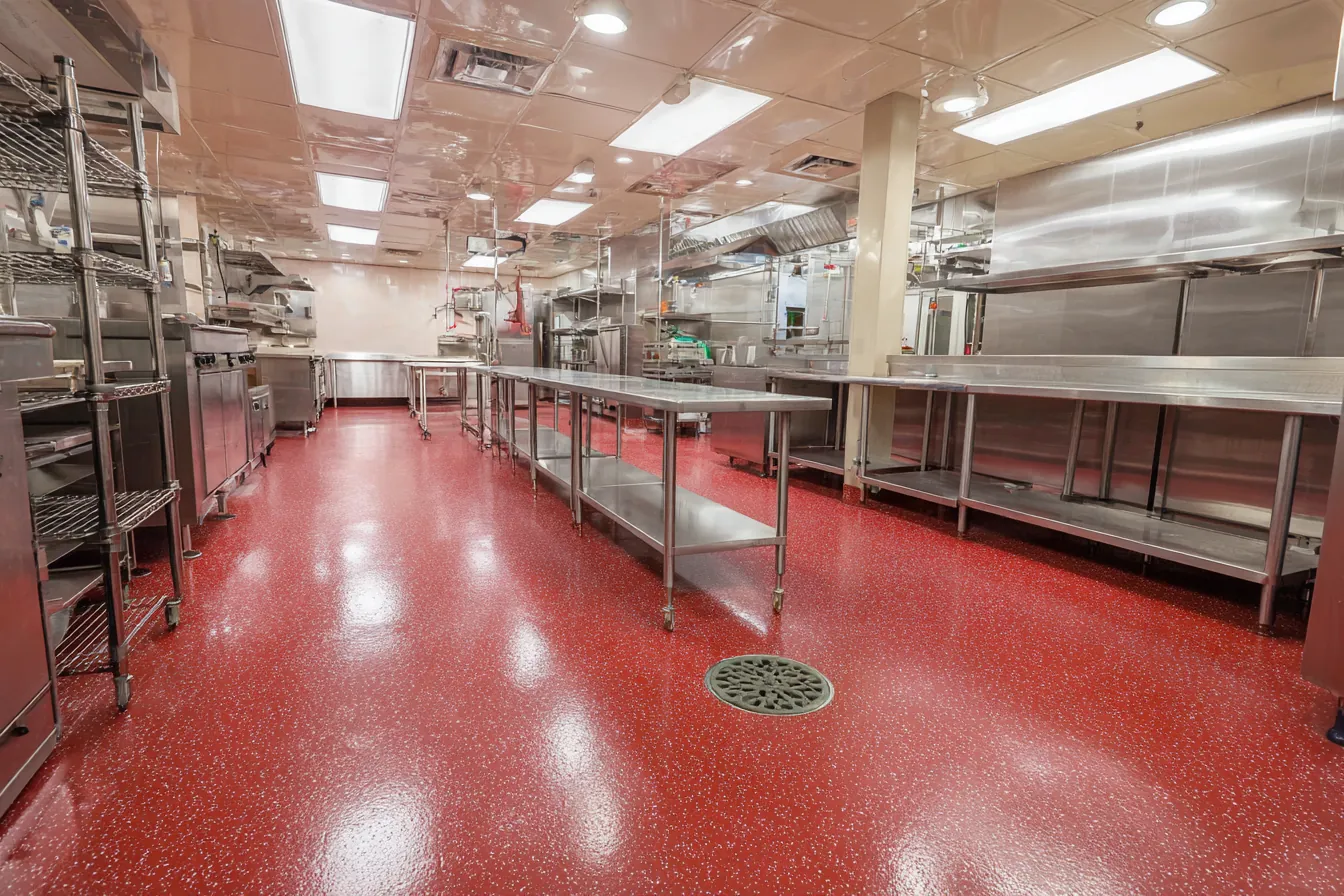 Empty commercial kitchen with a seamless speckled red resin floor that curves up into a coved wall base under stainless steel prep tables