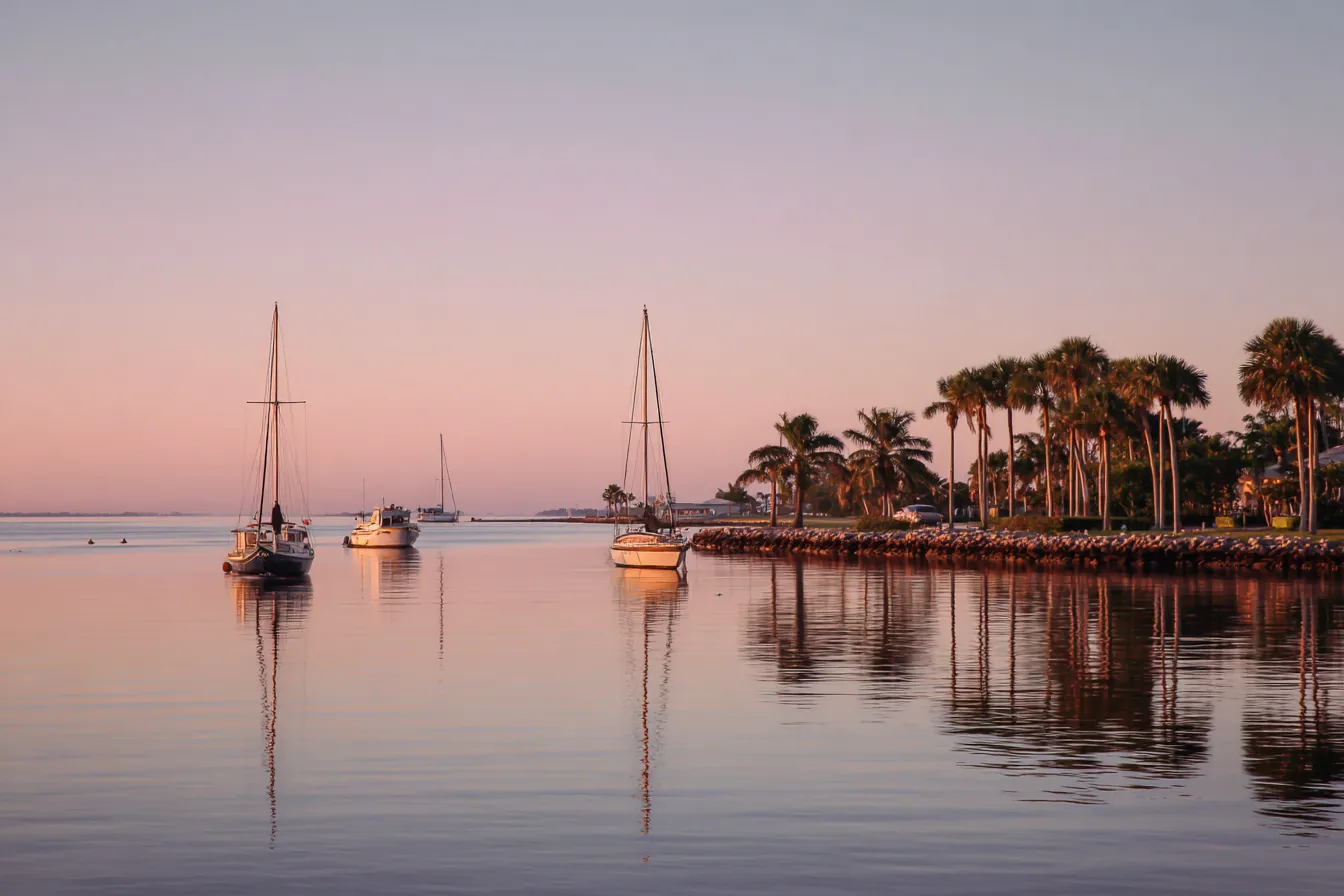 Sailboats moored on a calm Atlantic inlet at sunrise, palms along the far shore