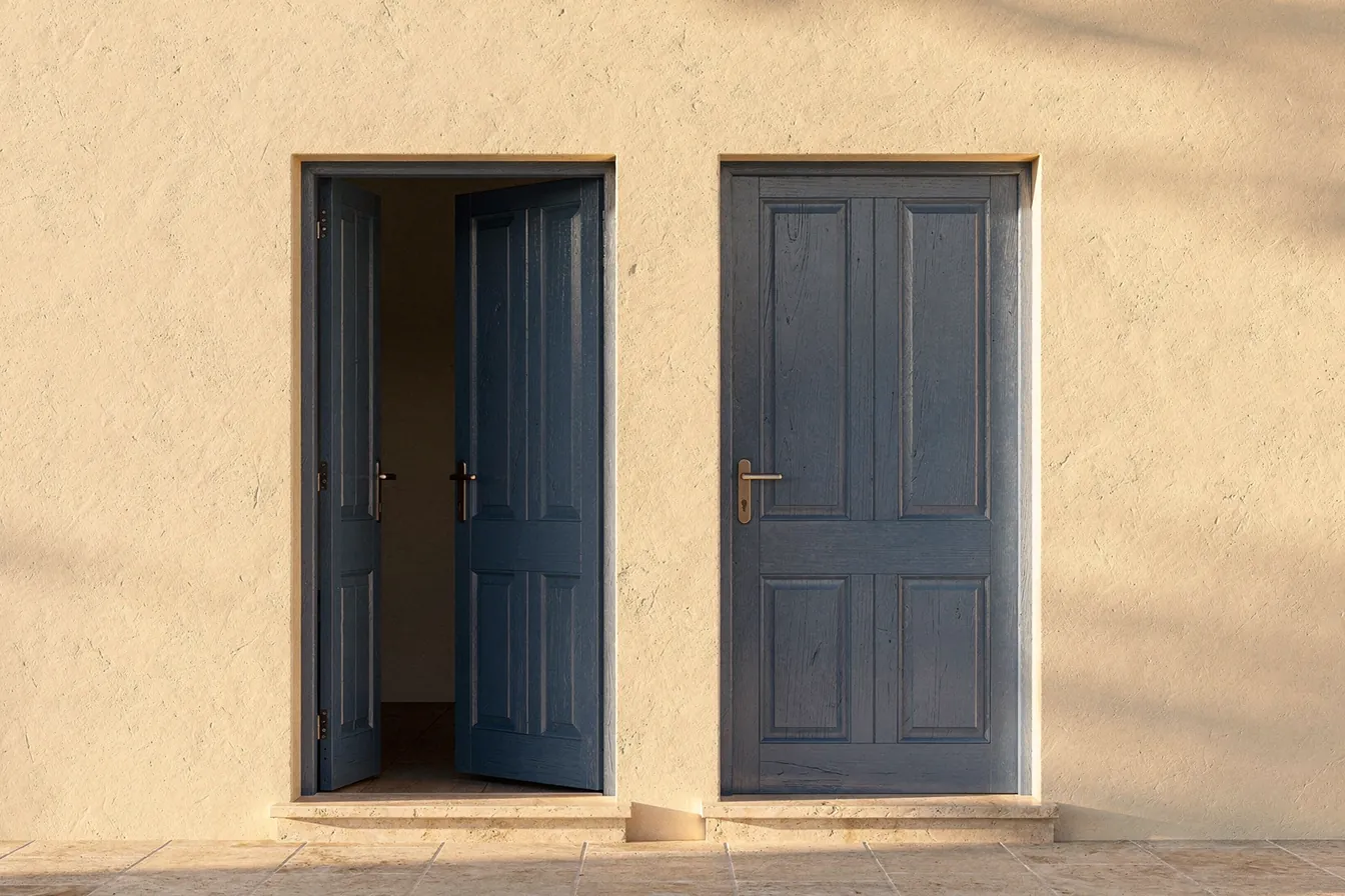 Two blue doors side by side in a cream stucco wall, one open and one closed, in afternoon light