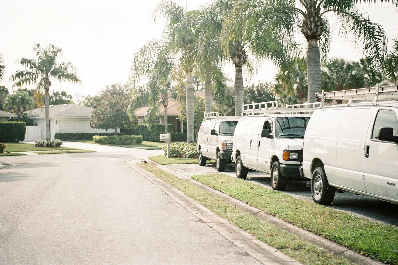 White work vans with ladder racks parked along a quiet palm-lined residential street