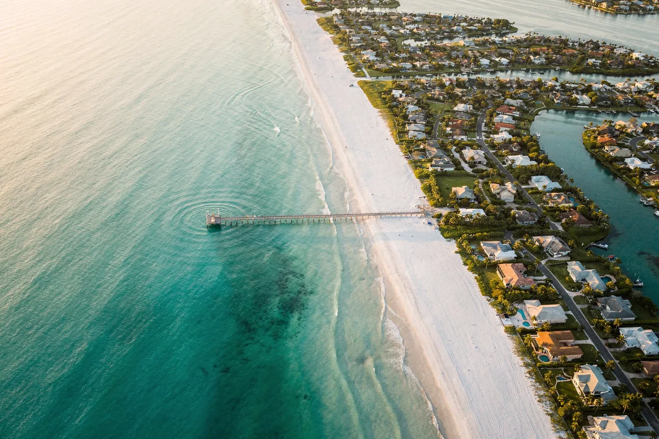 An aerial view of the Gulf coast at golden hour, a long white beach and a pier beside canal-front neighborhoods