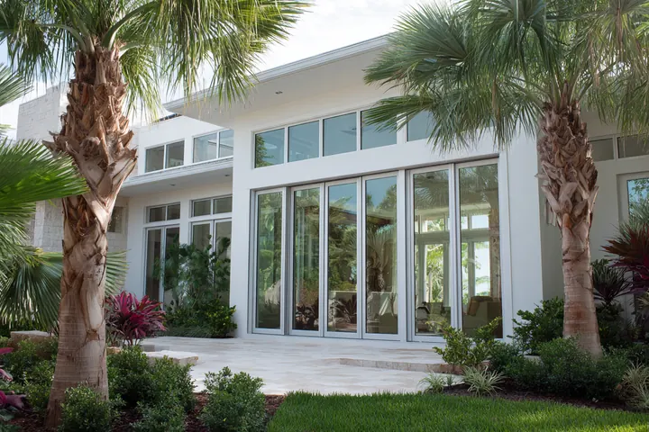 White Southwest Florida home with tall impact-rated glass doors and windows behind palms