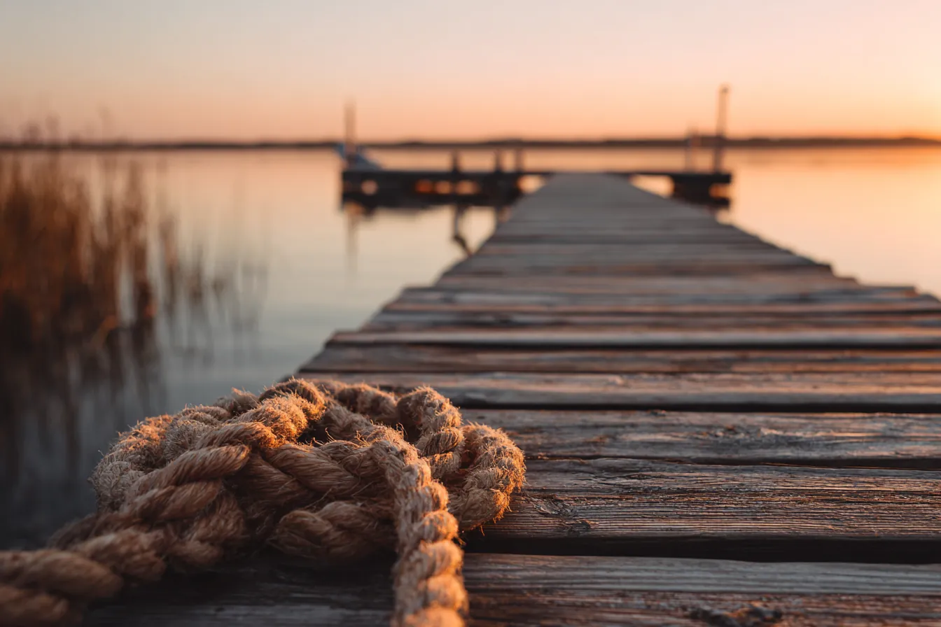 A wooden dock with a coiled rope reaching into calm water at sunrise