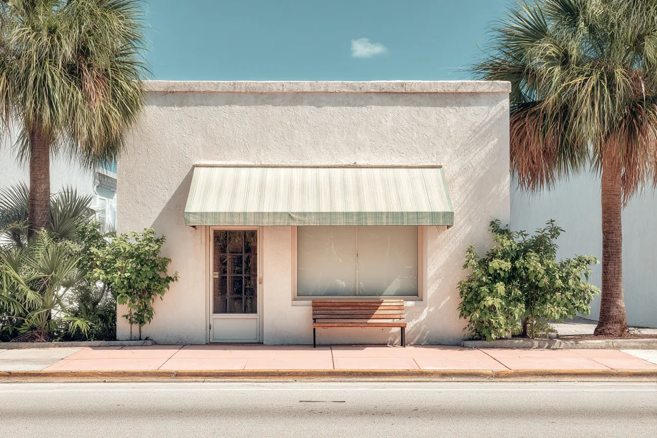 A small shop with a blank awning on a sunny Florida street corner, palms and a bench in front