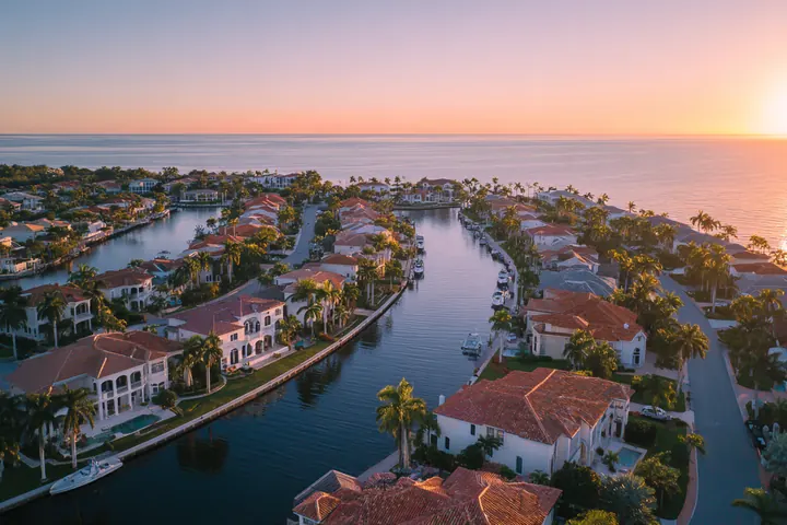 Golden-hour aerial view over a Southwest Florida coastal neighborhood of canals, tile roofs and palms, the Gulf beyond