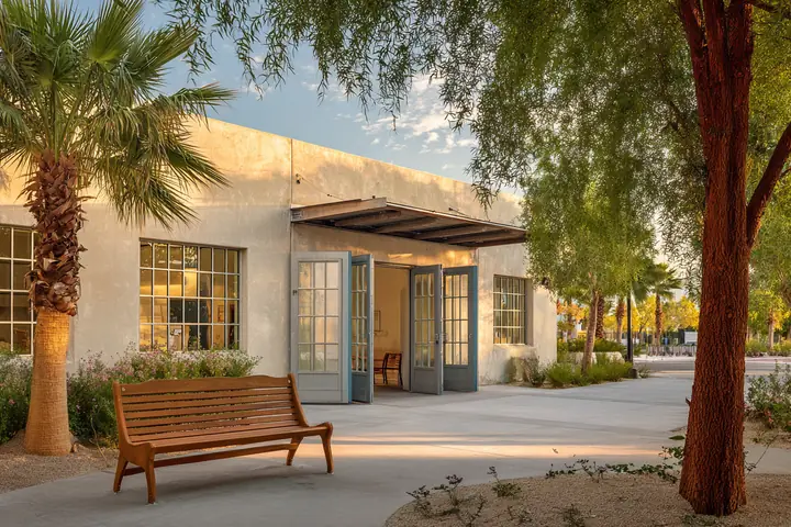 A community center in warm late afternoon light, an open double door and a bench under a shade tree
