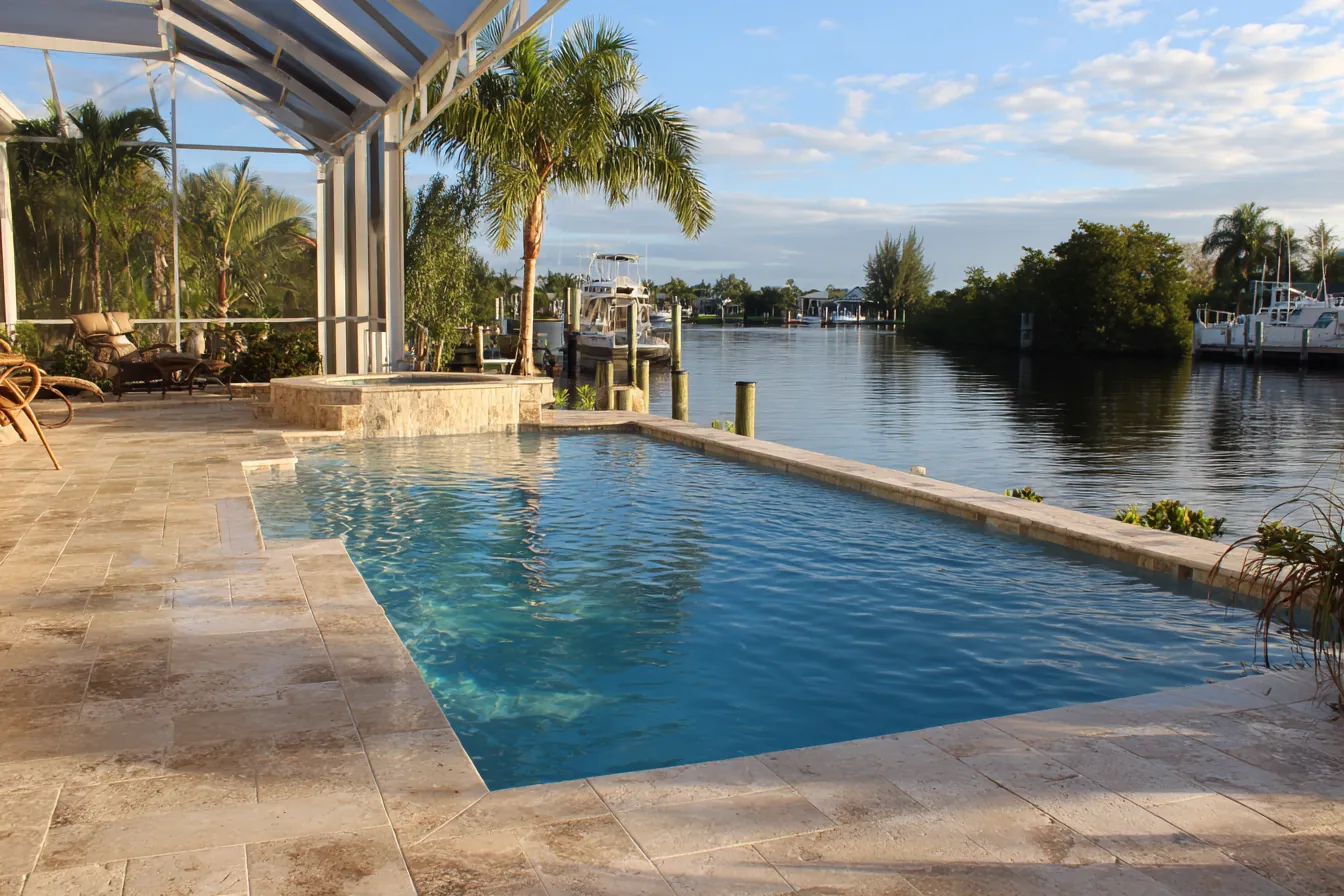 A travertine paver pool deck on a canal, with a seawall and calm water beyond