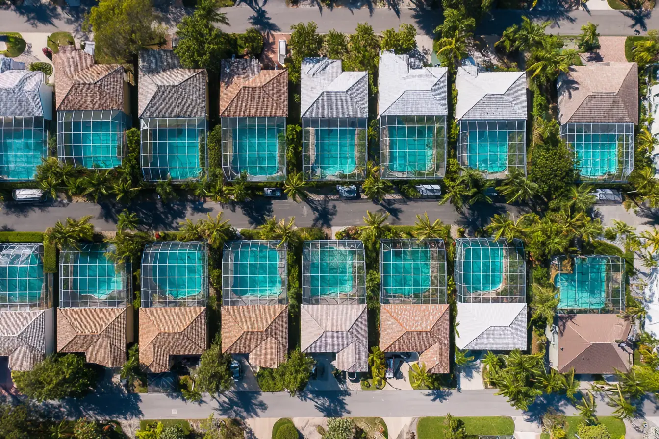 Neighboring Southwest Florida backyards seen from above, a row of blue pools under screen enclosures along one street