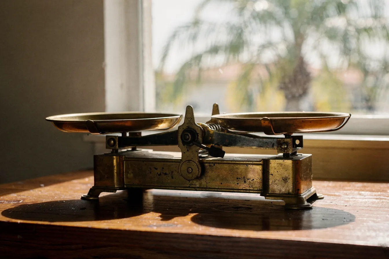 A brass balance scale on a wooden desk in warm window light