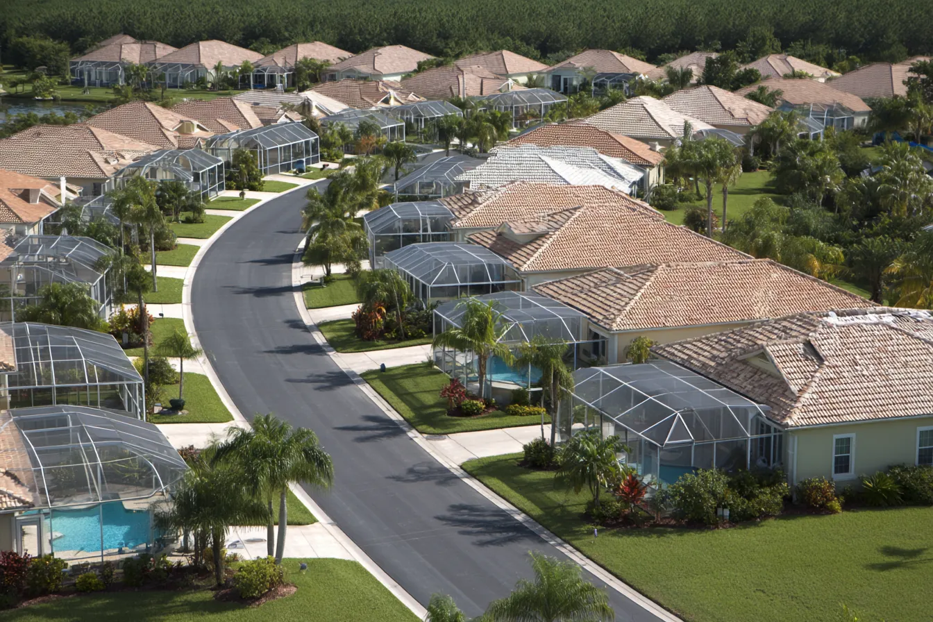 Aerial view of a curving Southwest Florida neighborhood street, tile-roofed homes each with a screened pool enclosure in the back yard