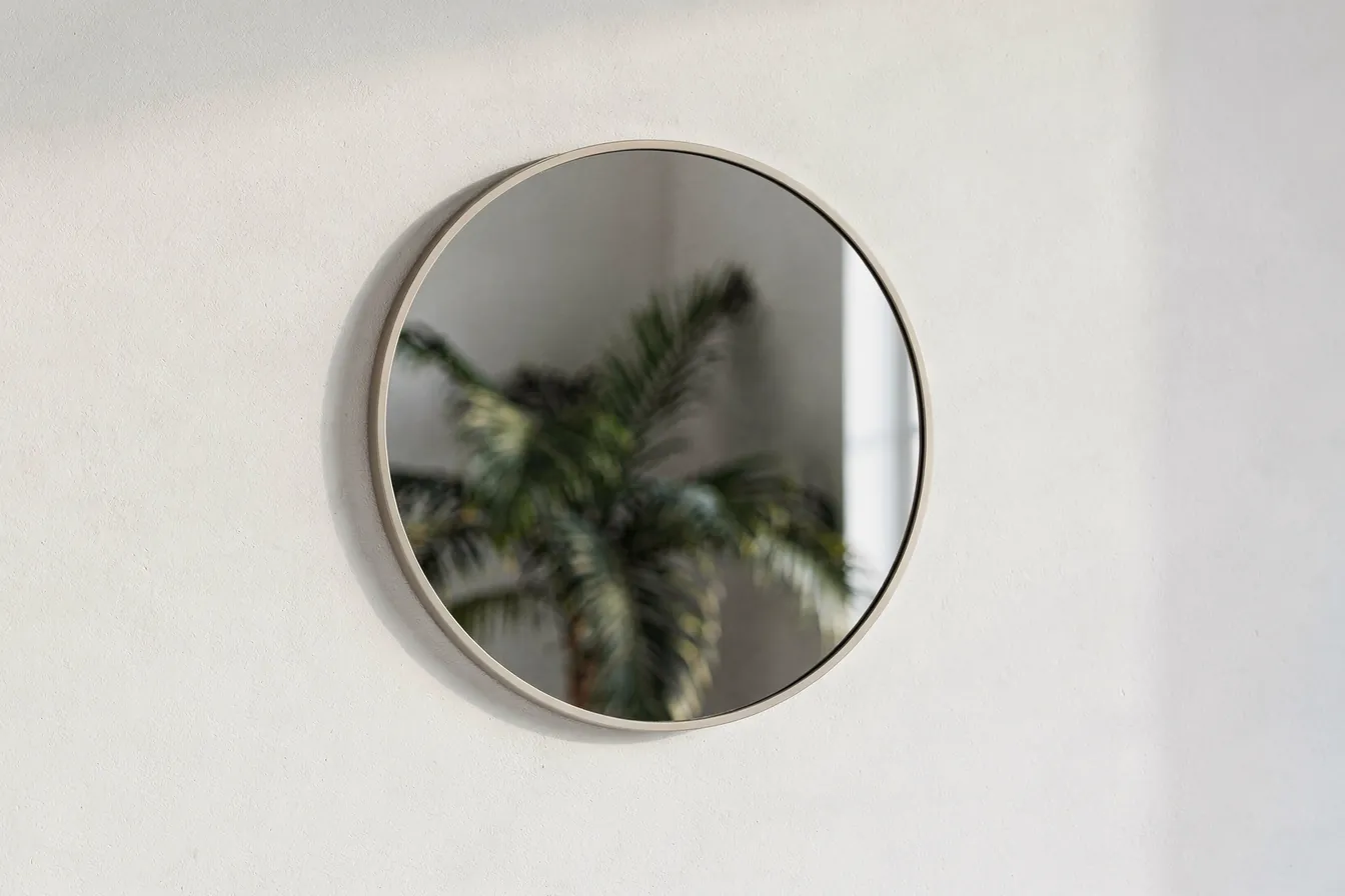 A round mirror on a white wall reflecting palms and soft window light