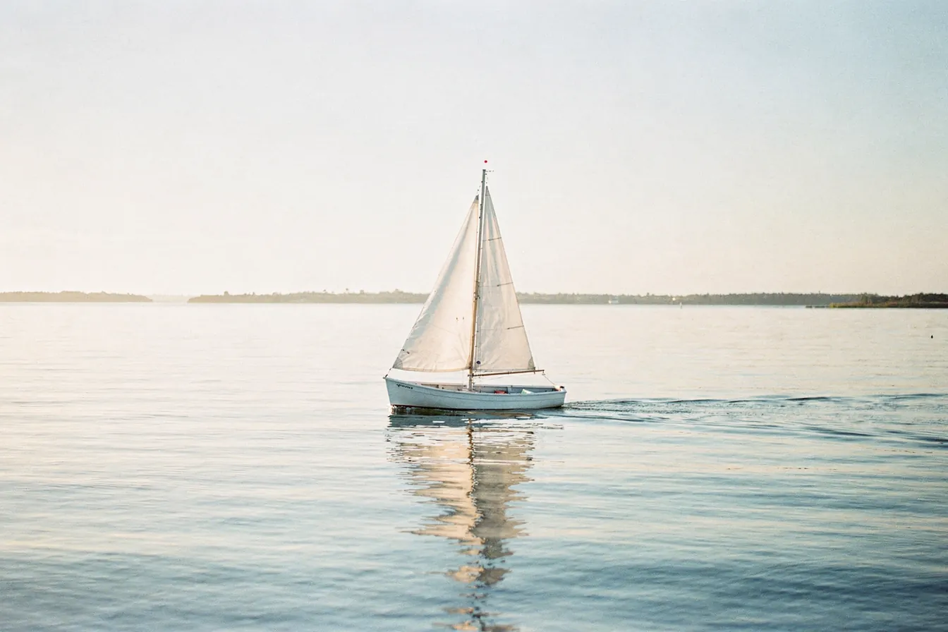 A small sailboat on open calm water in morning light