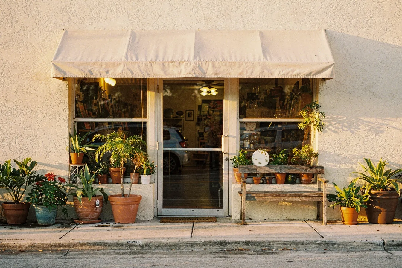 The front of a small independent shop at golden hour, a canvas awning over the door and potted plants along the walk