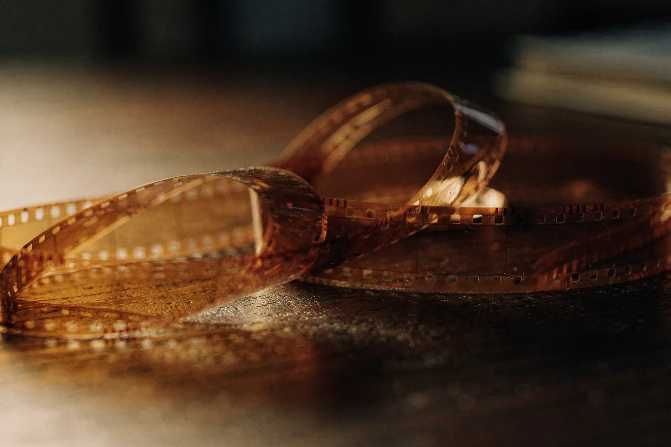 A coil of film unspooling across a dark wooden table in warm lamp light