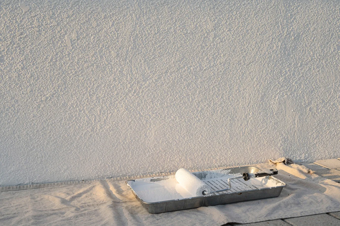 A freshly painted white stucco wall with a paint tray and roller on a drop cloth