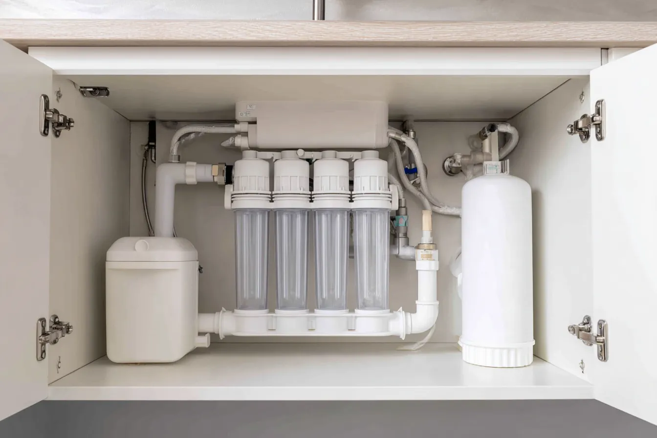 An under-sink reverse osmosis system with filter housings, a storage tank and tubing inside a white kitchen cabinet