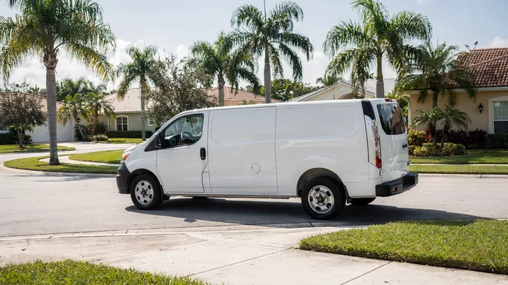 A white service van turning at the corner of a quiet palm-lined residential street