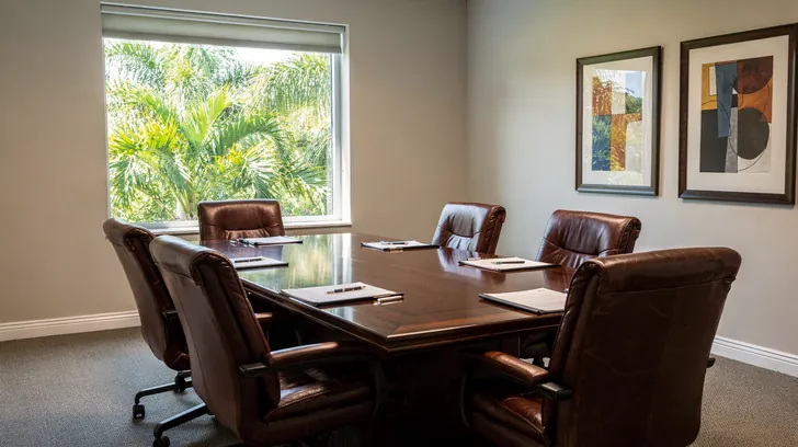 A small law office conference room with leather chairs around a wooden table and a window onto palms