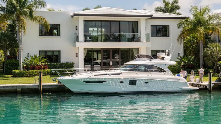 A white modern waterfront home with a motor yacht moored at its private dock on clear turquoise water