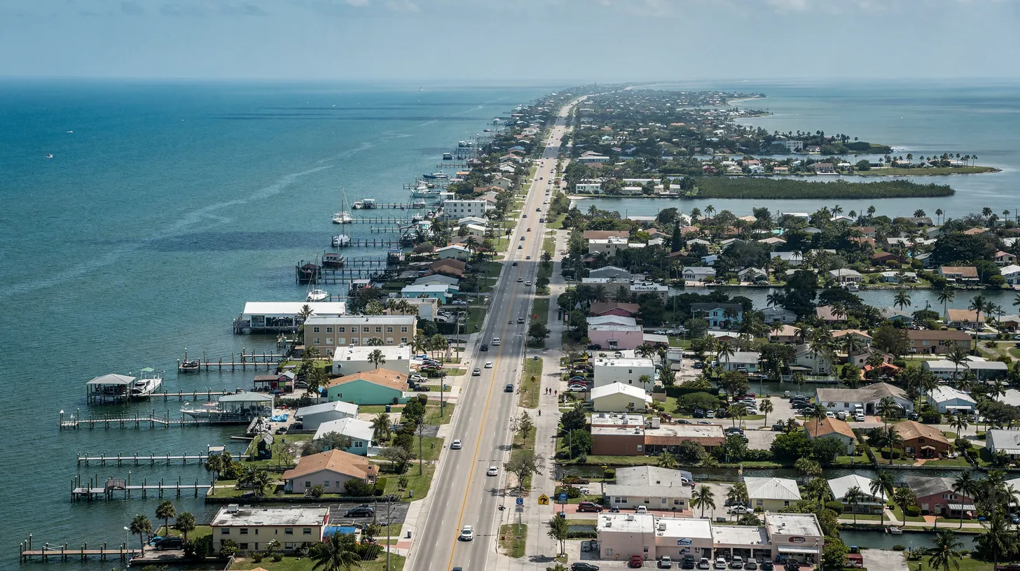 An aerial view of a long Gulf coast barrier island with a highway running its length past canals and homes