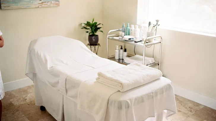 A made treatment bed with folded white towels in a bright, quiet med spa room