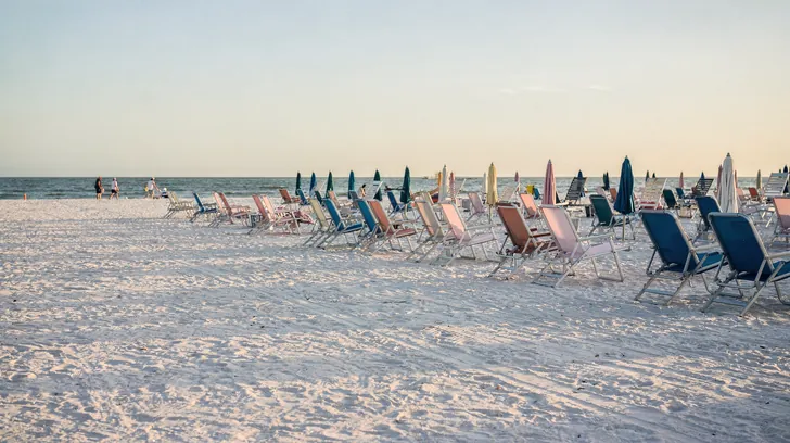 Rows of folded beach chairs and umbrellas on an almost empty white-sand beach in early morning
